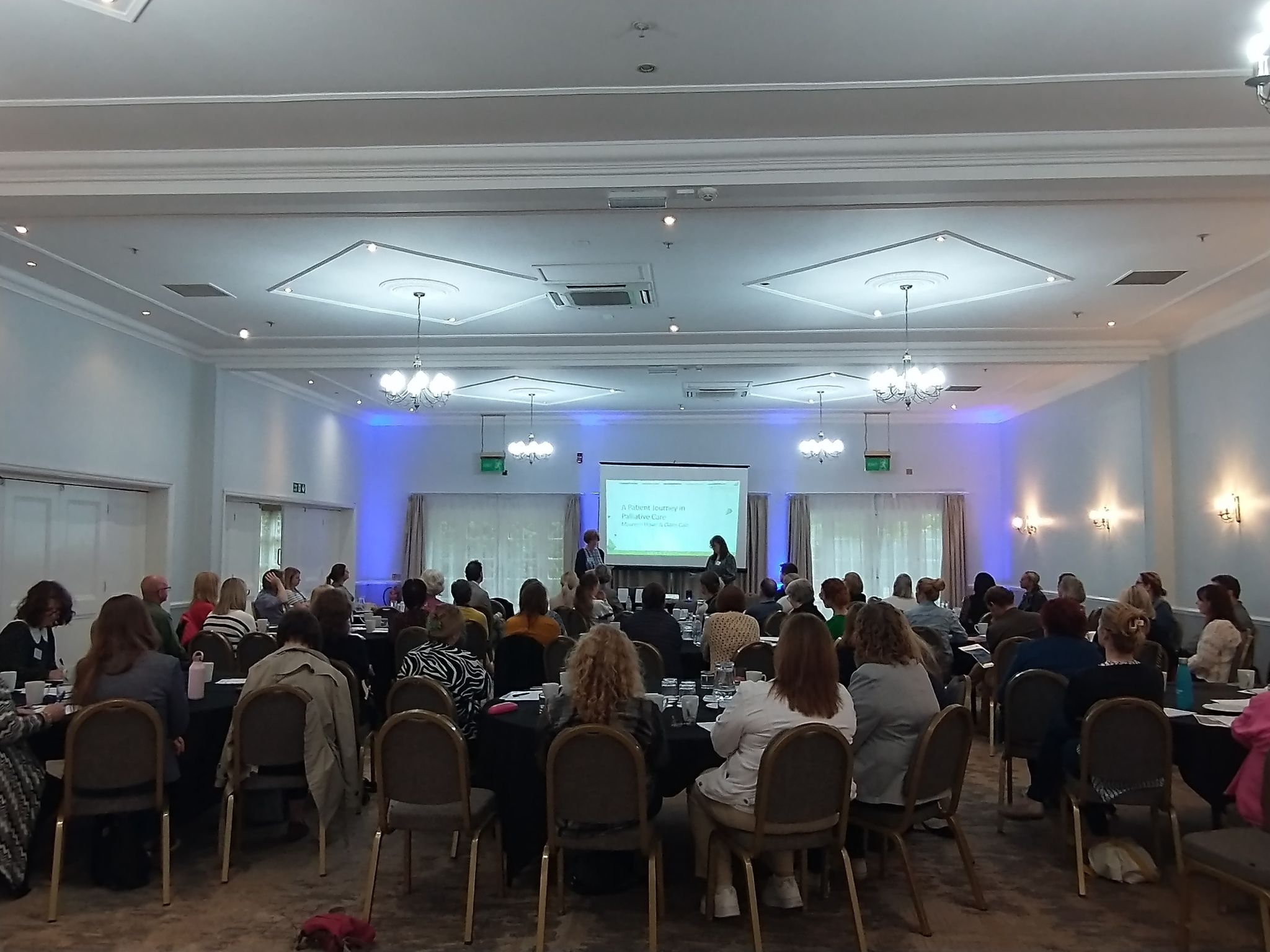 A couple of speakers hosting a conference to a big audience with an screen on the wall